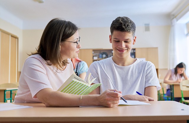 A pupil at a desk with a teacher helping